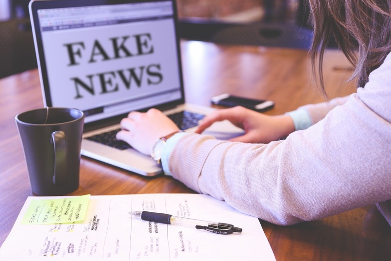 Nainen tietokoneen ääressä, jonka näytöllä lukee "fake news".